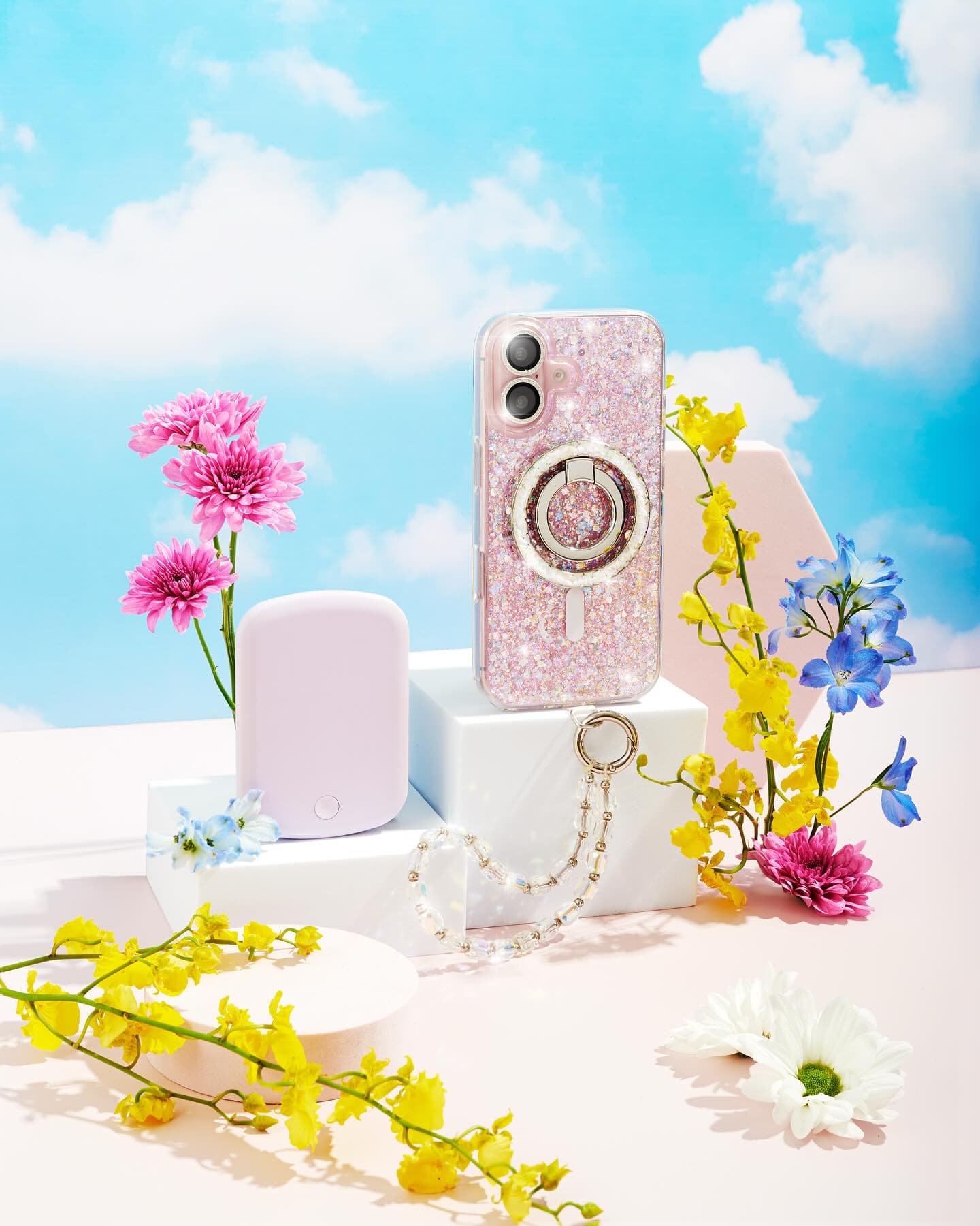 Glitter phone case styled with flowers on a sky-blue set